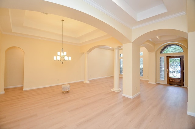 foyer entrance featuring an inviting chandelier, a raised ceiling, ornamental molding, light hardwood / wood-style floors, and decorative columns