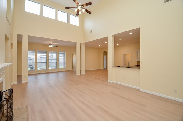 unfurnished living room with a tiled fireplace, ceiling fan, light hardwood / wood-style floors, and a high ceiling