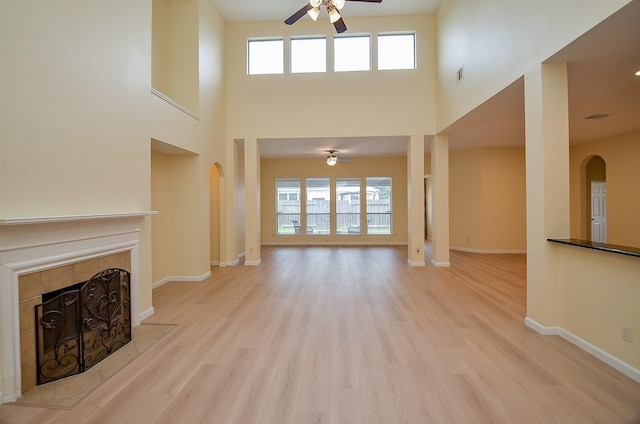 unfurnished living room with a high ceiling, light wood-type flooring, ceiling fan, and a tiled fireplace