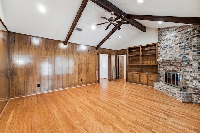 unfurnished living room featuring light wood-type flooring, ceiling fan, a fireplace, vaulted ceiling with beams, and wood walls