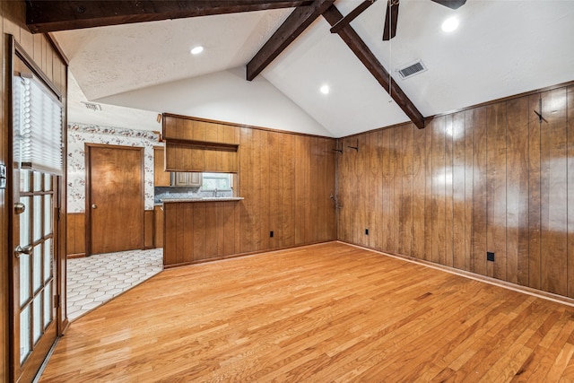 unfurnished living room with wood walls, vaulted ceiling with beams, ceiling fan, light wood-type flooring, and a wealth of natural light