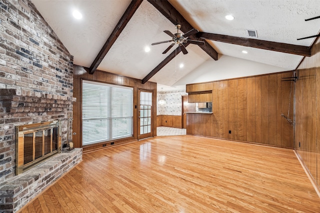 unfurnished living room with ceiling fan, vaulted ceiling with beams, wood walls, a textured ceiling, and a fireplace