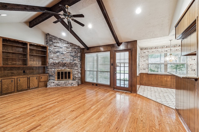 unfurnished living room featuring a brick fireplace, a textured ceiling, ceiling fan, lofted ceiling with beams, and wood walls