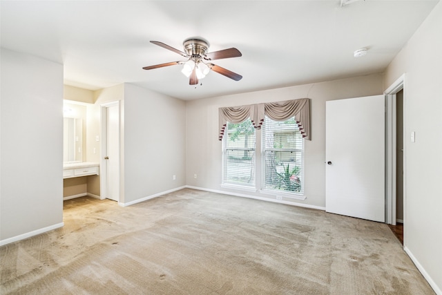 unfurnished bedroom featuring ceiling fan, built in desk, light carpet, and connected bathroom