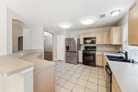 kitchen featuring sink, stainless steel fridge, light brown cabinetry, light tile patterned flooring, and range