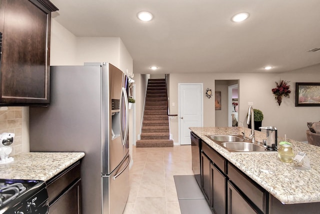 kitchen with light stone countertops, stainless steel appliances, sink, light tile patterned floors, and a center island with sink