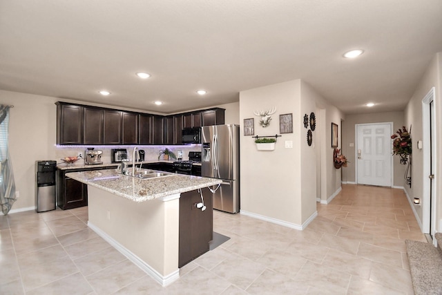 kitchen featuring light stone countertops, dark brown cabinets, a kitchen island with sink, sink, and black appliances