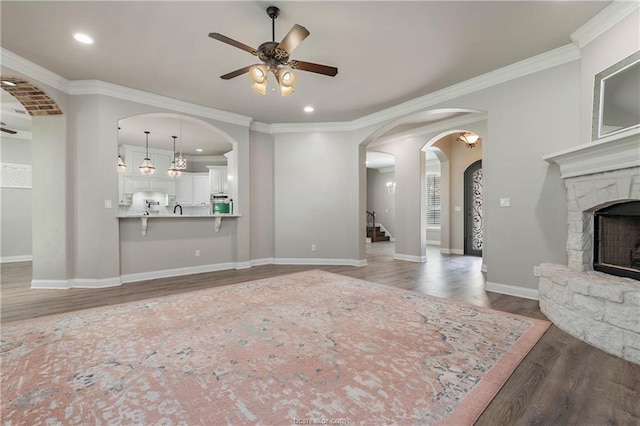 unfurnished living room with a stone fireplace, ceiling fan, crown molding, and dark hardwood / wood-style floors