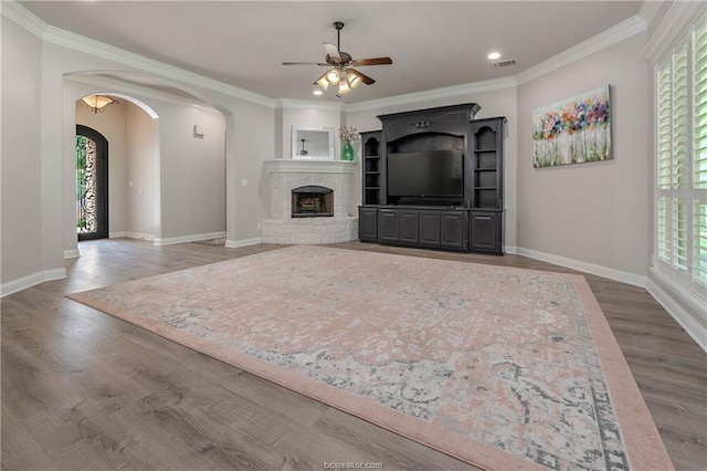 unfurnished living room featuring a stone fireplace, ceiling fan, hardwood / wood-style floors, and crown molding