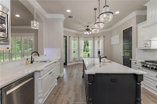 kitchen featuring a center island with sink, white cabinets, sink, decorative light fixtures, and light stone counters