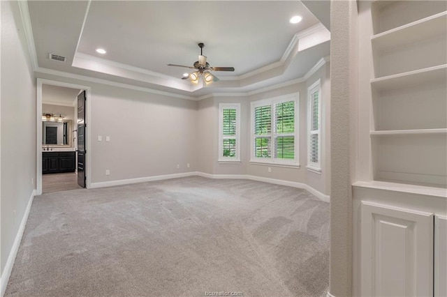 carpeted spare room with a raised ceiling, ceiling fan, and ornamental molding