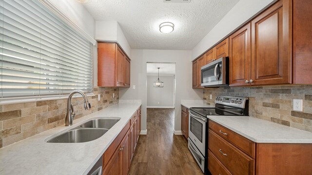 kitchen with backsplash, a textured ceiling, stainless steel appliances, sink, and pendant lighting