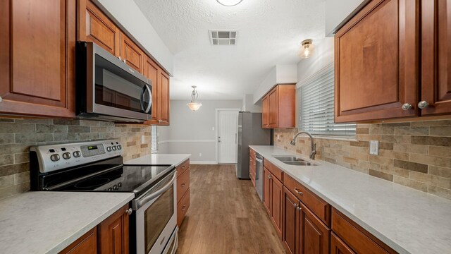 kitchen with sink, stainless steel appliances, decorative light fixtures, decorative backsplash, and light wood-type flooring