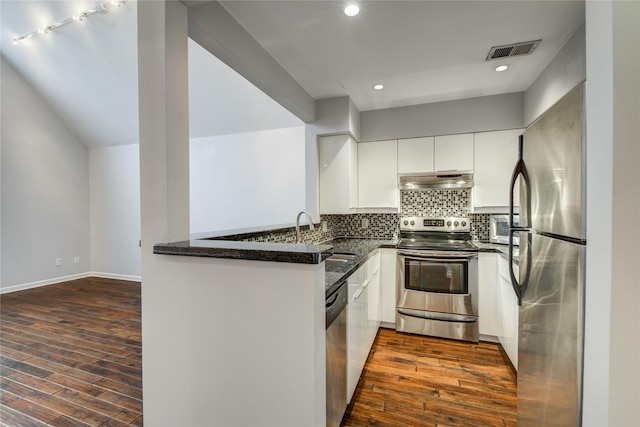 kitchen with dark stone countertops, kitchen peninsula, sink, stainless steel appliances, and white cabinets