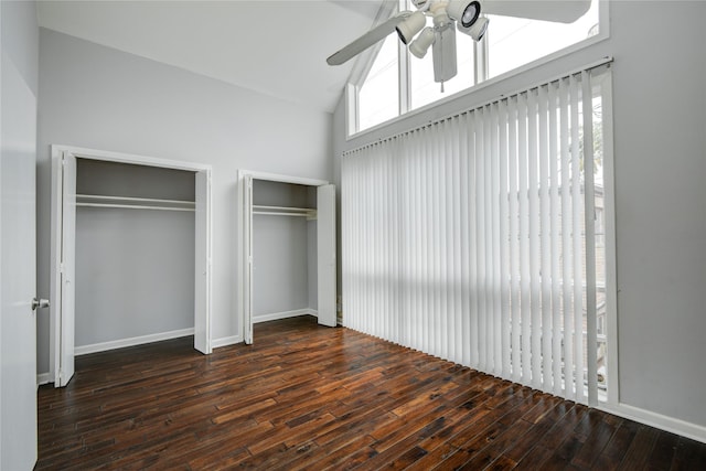 unfurnished bedroom featuring ceiling fan, two closets, dark hardwood / wood-style floors, and vaulted ceiling