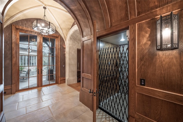 doorway with french doors, vaulted ceiling, an inviting chandelier, and wooden walls