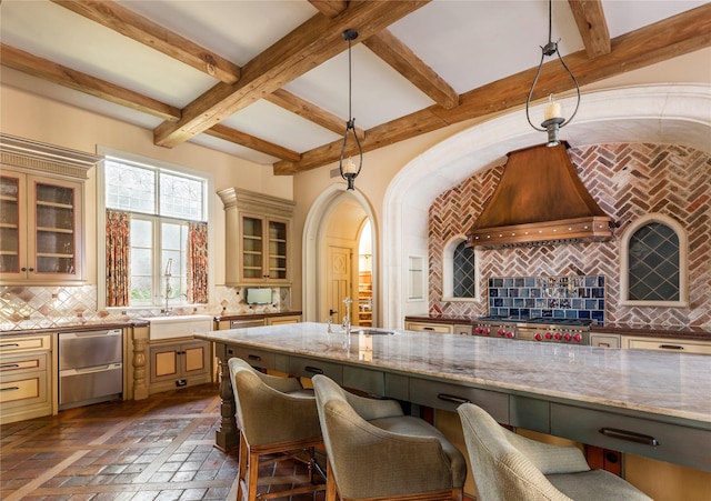 kitchen with backsplash, hanging light fixtures, stove, light stone counters, and custom range hood