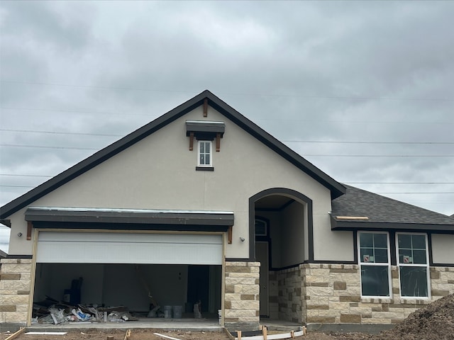 view of front facade featuring a shingled roof, stone siding, and stucco siding