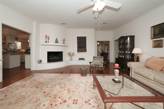 living room featuring ceiling fan, sink, a brick fireplace, dark hardwood / wood-style floors, and crown molding