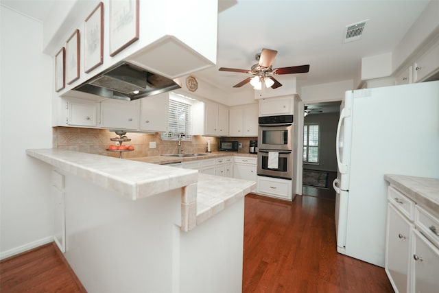 kitchen with white cabinets, white refrigerator, stainless steel double oven, and kitchen peninsula