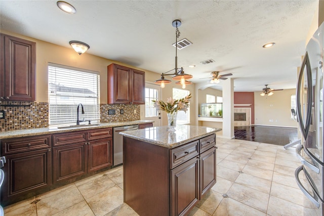 kitchen with stainless steel appliances, sink, a tile fireplace, pendant lighting, and a center island