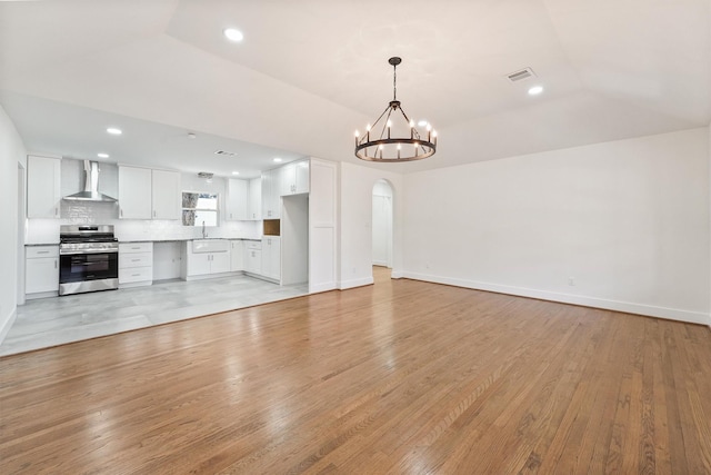 unfurnished living room with light wood-type flooring, vaulted ceiling, a chandelier, and sink