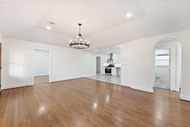 unfurnished living room with an inviting chandelier, light wood-type flooring, and vaulted ceiling