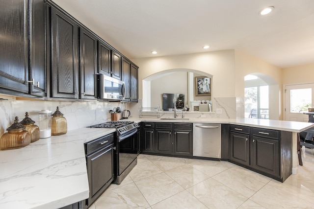 kitchen featuring kitchen peninsula, appliances with stainless steel finishes, light stone countertops, tasteful backsplash, and sink