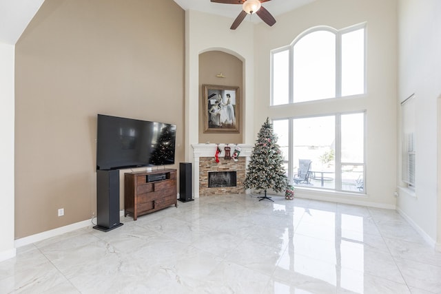 living room featuring a stone fireplace, ceiling fan, a healthy amount of sunlight, and a high ceiling