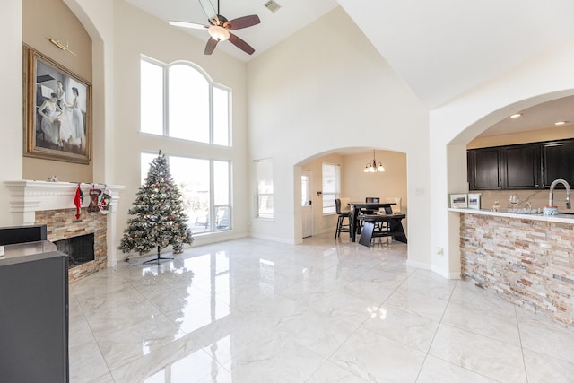 living room featuring ceiling fan with notable chandelier, a towering ceiling, and a stone fireplace