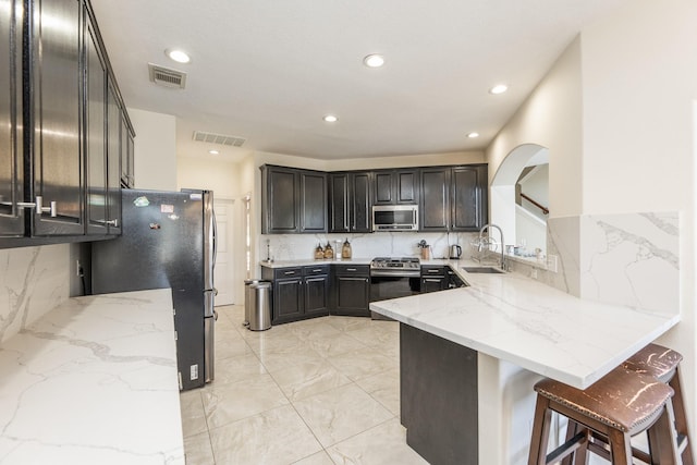 kitchen featuring sink, appliances with stainless steel finishes, tasteful backsplash, a kitchen bar, and kitchen peninsula