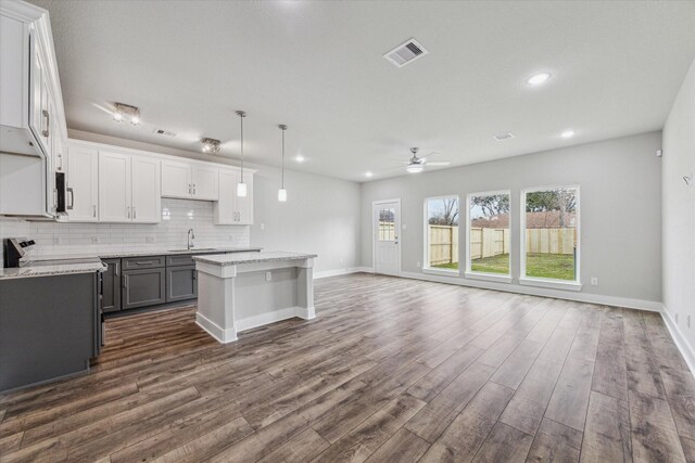 kitchen featuring light stone countertops, ceiling fan, sink, decorative light fixtures, and a center island