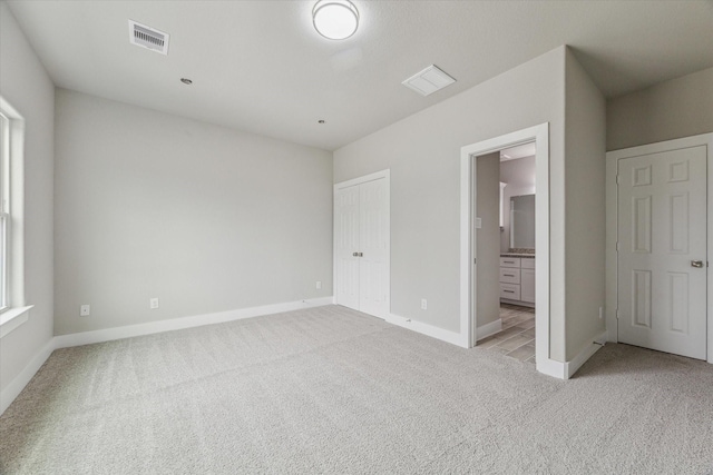 unfurnished bedroom featuring light colored carpet and connected bathroom