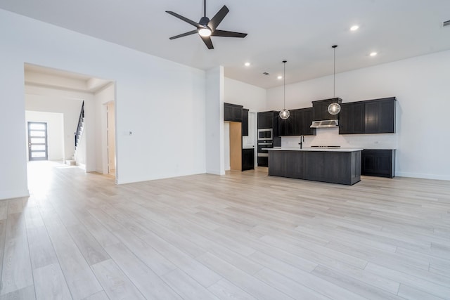 kitchen with hanging light fixtures, light hardwood / wood-style flooring, ceiling fan, decorative backsplash, and an island with sink