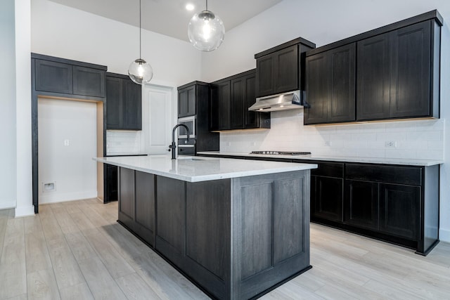 kitchen featuring light wood-type flooring, stainless steel gas cooktop, hanging light fixtures, and an island with sink