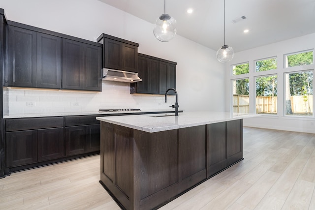 kitchen with decorative backsplash, stainless steel gas cooktop, sink, hanging light fixtures, and an island with sink