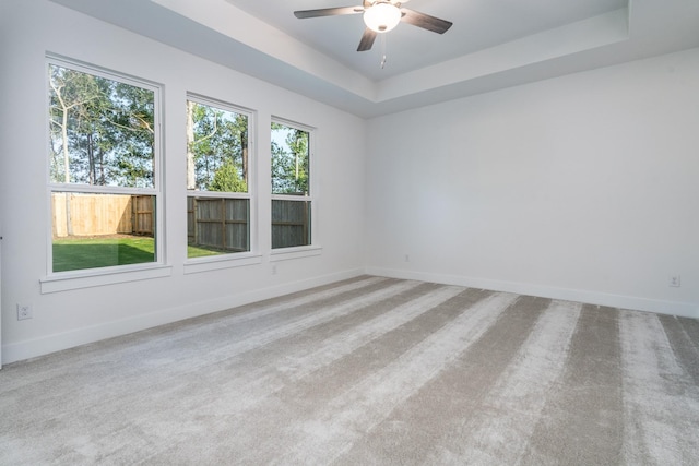 empty room featuring ceiling fan, a raised ceiling, and light carpet