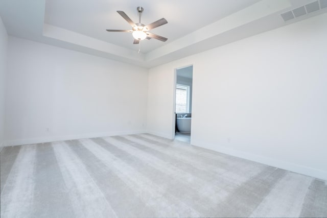 empty room with light colored carpet, a raised ceiling, and ceiling fan