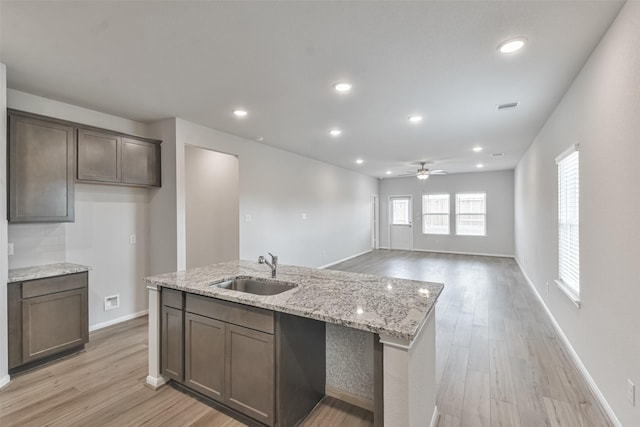 kitchen featuring light stone countertops, light wood-type flooring, a kitchen island with sink, ceiling fan, and sink