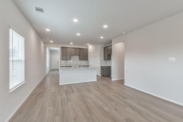 kitchen with light stone countertops, decorative backsplash, light wood-type flooring, sink, and an island with sink