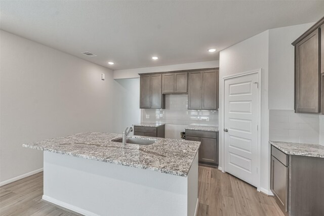 kitchen featuring decorative backsplash, light hardwood / wood-style flooring, a kitchen island with sink, and sink