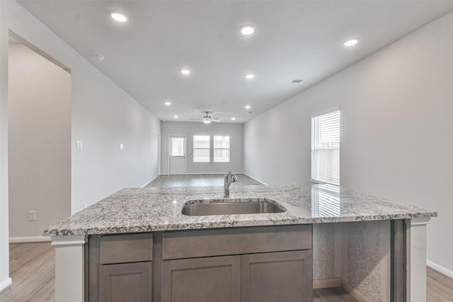 kitchen featuring ceiling fan, sink, light stone countertops, and light hardwood / wood-style floors