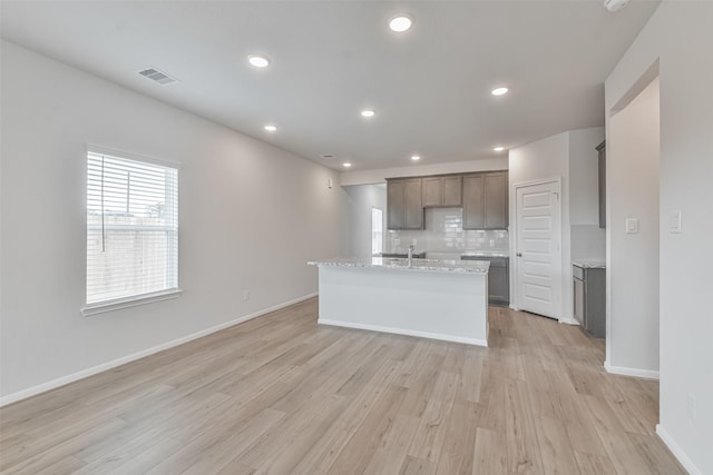 kitchen with sink, light stone counters, backsplash, an island with sink, and light hardwood / wood-style floors