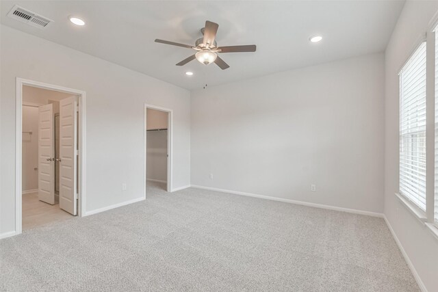 unfurnished bedroom with ensuite bathroom, light colored carpet, ceiling fan, a spacious closet, and multiple windows