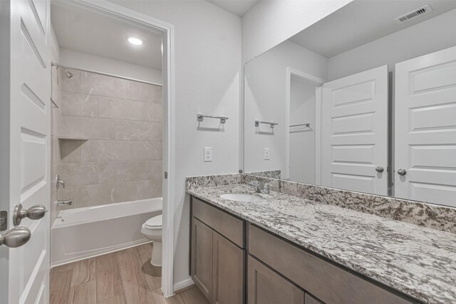 full bathroom featuring hardwood / wood-style flooring, vanity, toilet, and tiled shower / bath combo