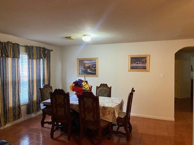 dining space with dark tile patterned floors, baseboards, visible vents, and arched walkways