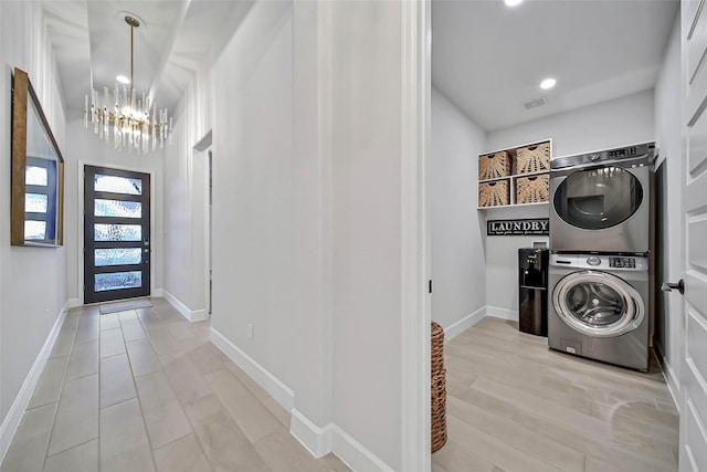 clothes washing area with light wood-type flooring, an inviting chandelier, and stacked washer / drying machine