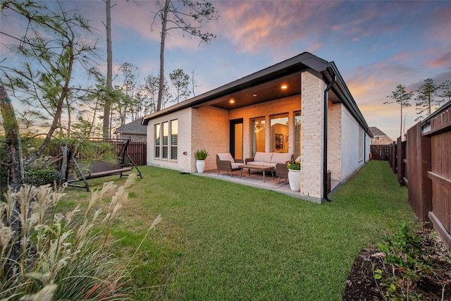 back house at dusk featuring an outdoor hangout area, a patio, and a yard