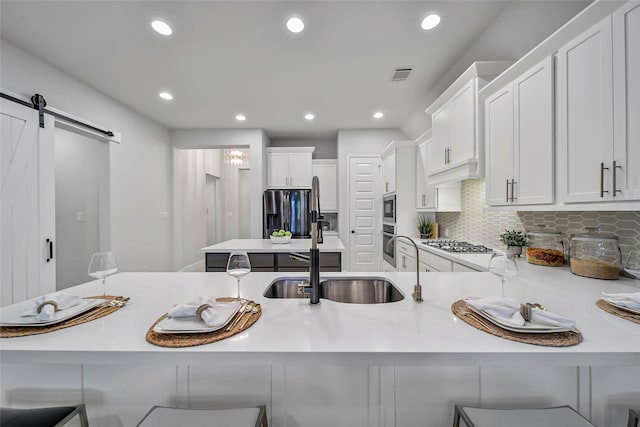 kitchen featuring a kitchen breakfast bar, stainless steel appliances, sink, a barn door, and white cabinetry