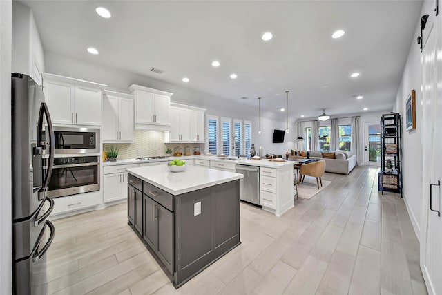 kitchen with white cabinets, stainless steel appliances, a kitchen island, and hanging light fixtures